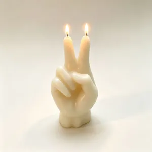 Primo piano di una candela a forma di mano con segno della pace accesa in crema