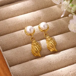 Close-up of ocean-style gold conch shell earrings with white pearl detail on beige linen.