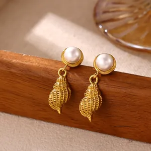 Macro detail view showing textures of gold ocean conch earrings with white pearl studs