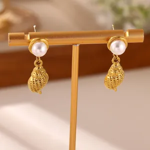 Macro view of ocean-inspired golden conch shell drop earrings with white pearl studs
