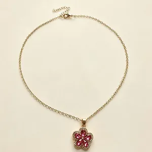 Primo piano di elegante collana dorata con ciondolo a fiore in cristallo rosa e pavé.
