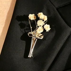 Elegant silver vase brooch with white dried flowers pinned on a black suit lapel.