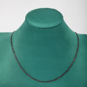 Detailed macro view of dark stainless steel 3:1 Figaro chain on green velvet display