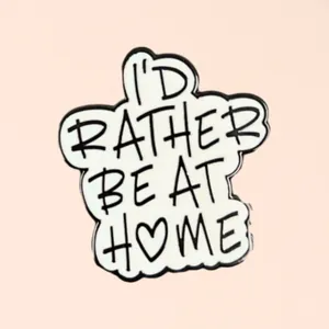 Gros plan sur un pin's en émail 'I'd Rather Be At Home' avec un détail de cœur