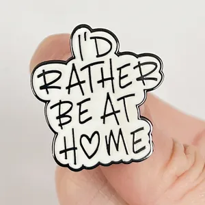Gros plan d'un pin's en émail blanc avec le texte I'd Rather Be At Home et un cœur