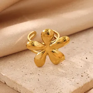 Macro view of a gold flower-shaped stainless steel ring on a textured stone surface.