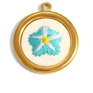 Détail d'un pendentif rond en acier doré avec une fleur bleue brodée