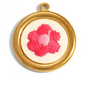 Vue détaillée d'un pendentif rond en acier inoxydable doré avec fleur brodée rose