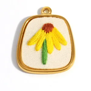 Détail d'un pendentif en forme de fleur brodée jaune avec un cadre en acier doré poli.
