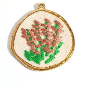 Détail macro d'un pendentif brodé de fleurs champêtres avec un cadre doré en inox