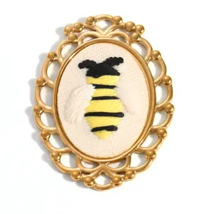 Vue détaillée d'un pendentif vintage en acier inoxydable doré avec une broderie d'abeille