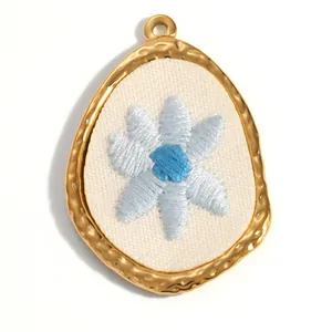 Détail macro d'une fleur brodée délicate sur un pendentif en acier inoxydable doré