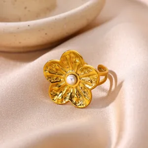 Close-up of golden stainless steel flower ring with central pearl on silk background.