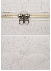 Detail of shell quilted stitching and dual metal zippers on a white cosmetic bag