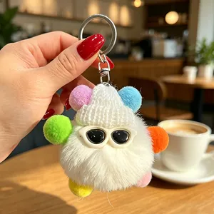 Primo piano di un portachiavi a mostro di peluche bianco con pompon colorati e occhiali