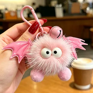 Primo piano di un portachiavi a mostro rosa peloso con ali di pipistrello e un campanellino rosa.