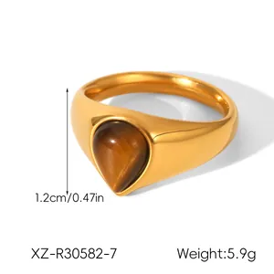 Detalle de anillo de acero de titanio dorado con piedra de ojo de tigre en gota