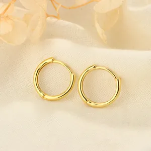 Primer plano de pendientes de aro minimalistas en plata S925 bañada en oro sobre tela clara.