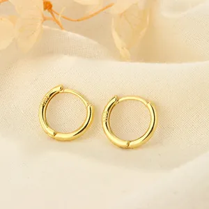 Primer plano de pendientes de aro minimalistas de plata S925 bañados en oro sobre tela