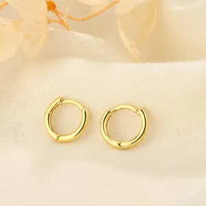 Primer plano de pendientes de aro minimalistas de plata S925 chapados en oro sobre tela.