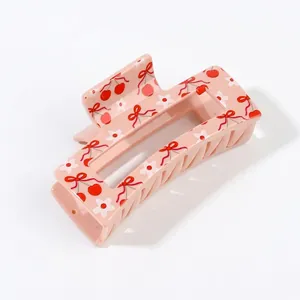 Detailed view of a pink hair claw clip featuring red cherry, bow and flower patterns