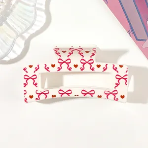 Close-up detail of a white hair claw clip with pink bow and red heart patterns