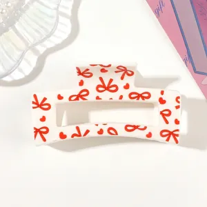 Detail of white claw clip featuring a vibrant red bow and heart pattern design