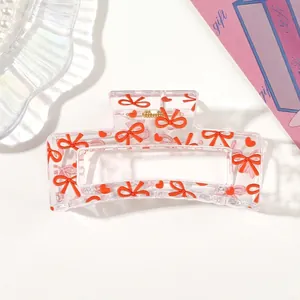 Close-up of transparent hair claw clip with red bow and heart patterns.