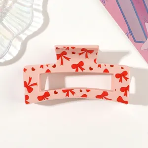 Close-up of pink square hair claw clip with red bow and heart pattern prints