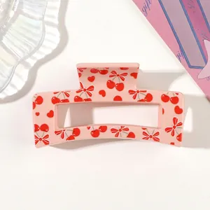Close-up detail of a pink hair claw clip featuring a cute red cherry and bow tie print pattern