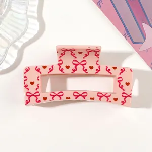 Detailed view of a pink hair claw clip featuring cute red heart and bow ribbon patterns