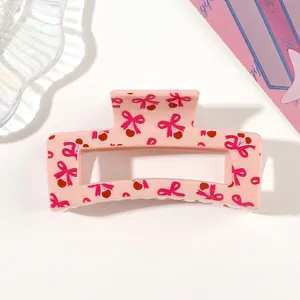 Detailed macro view of pink rectangular hair claw clip with cute cherry and bow pattern.