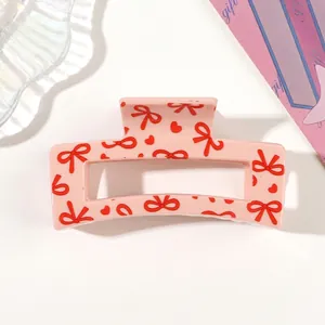 Detailed macro view of a pink hair claw clip featuring red bow and heart patterns
