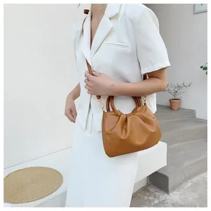 Stylish brown pleated cloud bag with wooden handles shown on model in white outfit