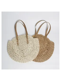 Detail of two round bohemian straw beach bags in cream and beige with leather handles.
