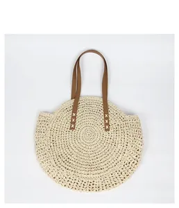 Detail view of a round bohemian straw woven bag featuring contrast brown faux leather straps