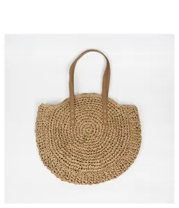 Detail view of a round bohemian straw woven summer tote bag with brown shoulder straps.
