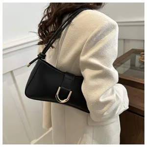 Detail of a chic black underarm bag with gold buckle on a beige blazer model.