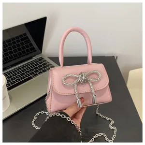 Detalle de un mini bolso rosa con un lazo de diamantes de imitación y correa de cadena plata