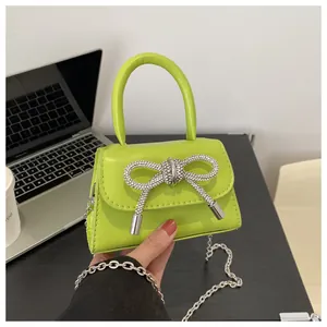 Primer plano de un mini bolso verde lima adornado con un brillante lazo de strass.