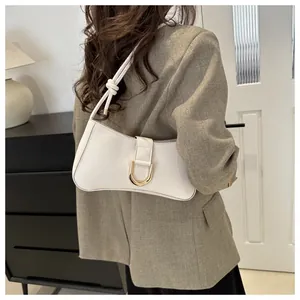 Detail of white underarm bag with gold horseshoe buckle and knotted strap on model.