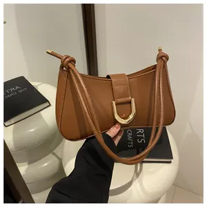 Close-up of a brown leather axillary bag with a gold D-ring buckle on a white table.