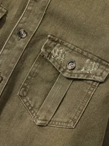 Nahaufnahme der abgenutzten Tasche an einem olivgrünen Herren-Jeanshemd im Workwear-Stil