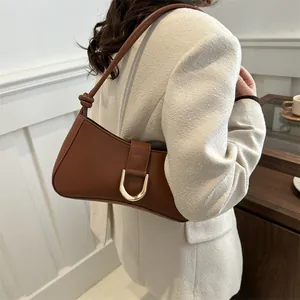 Minimalist chic brown leather underarm bag with elegant gold buckle on white blazer.