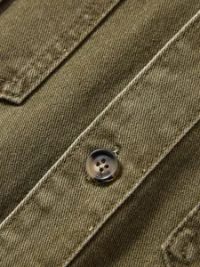 Nahaufnahme eines olivgrünen Arbeitshemds mit Stoffstruktur und Knopfdetails.