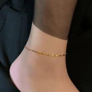 Detailaufnahme einer zierlichen vergoldeten Titanstahl-Fußkette am Knöchel
