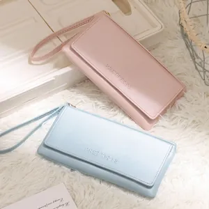 Detail view of pink and blue long wallets with wrist straps and embossed logo on white fur.
