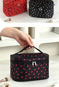 Macro view of a portable black cosmetic bag with pink hearts and a hand holding the handle