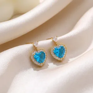Detailed close-up of gold heart earrings with sparkling blue zircon and silk background