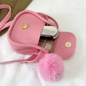 Borsa a tracolla mini a sella rosa con pompon peloso per contenere i cosmetici.